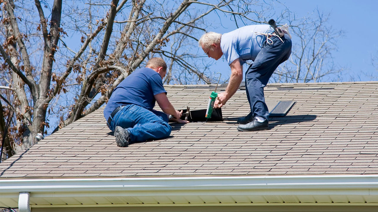 Two people repairing a leak on a shingle roof