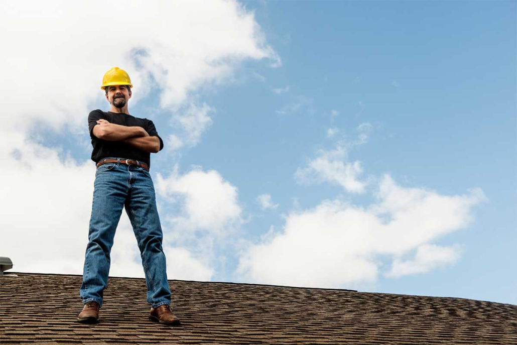 A man stands confidently on the roof of a house, overlooking the surroundings with a thoughtful expression.