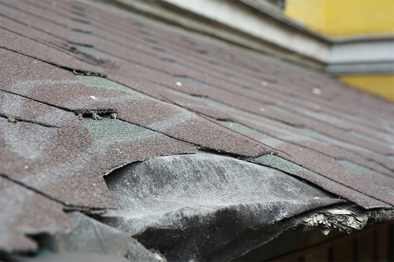 A damaged roof featuring a hole and a broken shingle, indicating potential water leakage and structural issues