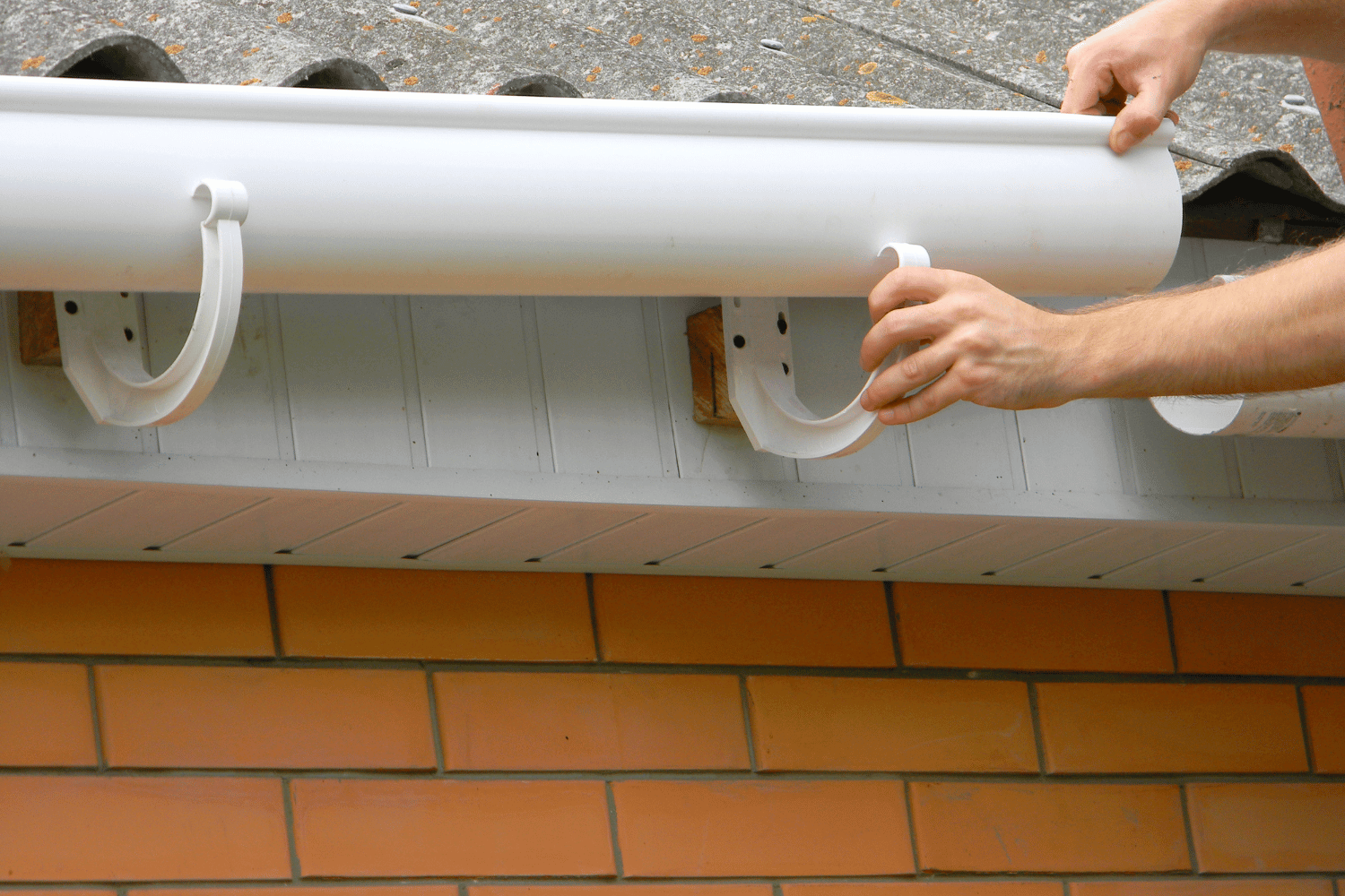 A roofing contractor working on a roof while discussing the installation of gutters. 